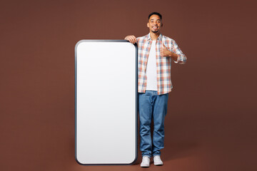 Wall Mural - Full body young happy man of African American ethnicity he wear blue shirt casual clothes big huge blank screen mobile cell phone smartphone with area show thumb up isolated on plain brown background.