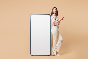 Poster - Full body young smiling woman she wear white top casual clothes big huge blank screen mobile cell phone with area using smartphone isolated on plain pastel light beige background. Lifestyle concept.