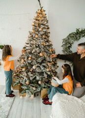 Wall Mural - A father and his two daughters joyfully decorate a snow-flocked Christmas tree adorned with warm lights and golden ornaments. The scene is filled with holiday cheer and familial love