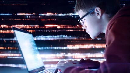 A young person sits focused on a laptop, typing intently as colorful lights illuminate the dark environment. The atmosphere suggests a late-night coding session filled with creativity