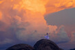 © Connect Images - A woman in a white dress stands triumphant atop a rock formation under a vibrant sunset sky, USA