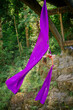 © Connect Images - Aerial artist performing an inverted pose on purple silk fabric suspended from a wooden structure in a forested area, USA