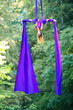 © Connect Images - Aerial silk performer doing an inverted split in a lush green forest setting, USA