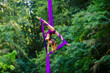 © Connect Images - Aerial silk performer executing a pose in purple fabric amidst lush greenery, USA