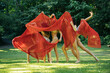 © Connect Images - A group of five dancers moves gracefully with a flowing red fabric in a sunlit park setting, USA