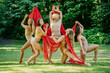 © Connect Images - Five dancers clad in natural tones perform a choreographed piece with flowing red fabric in an outdoor, grassy setting, USA