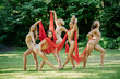 © Connect Images - Five dancers in bodysuits perform an expressive dance with red fabric in a sunlit park, USA