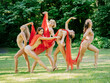 © Connect Images - Group of five dancers in nude outfits with red scarves performing an elegant dance routine in a sunlit park, USA