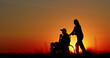 © StockMediaSeller - Silhouette of a person pushing a wheelchair during a vibrant sunset, symbolizing care, assistance, and support in a tranquil rural setting. The golden sky enhances the emotional warmth.