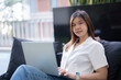 © Tj - Young asian freelancer woman is working on a laptop while sitting comfortably on an outdoor terrace, enjoying the fresh air and natural light as she focuses on her tasks