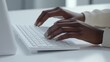 © mbah - Close-up of dark-skinned hands typing on a white wireless keyboard.