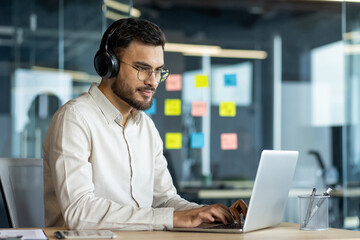 businessman wearing headphones works diligently on a laptop in a modern office. surrounded by sticky