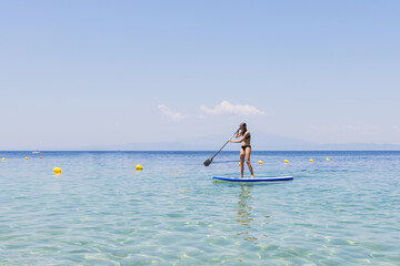 Wall Mural - Young girl paddleboarding in clear water on a summer vacation.