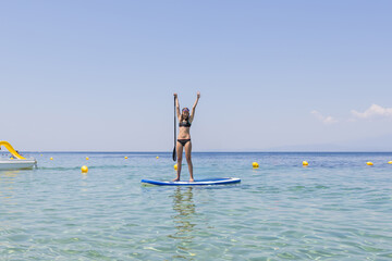 Wall Mural - Young girl paddleboarding in clear water on a summer vacation.