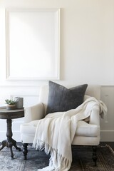 Canvas Print - A blank white frame hanging above a corner armchair, surrounded by a throw blanket and a small side table. 