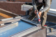 © Jelena - Construction worker using silicone sealant adhesive to fix a metal sheet on the skylight window. A roofer and window master work.