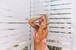 © svetograph - A woman in a bikini stands in front of a white shower stall. She is smiling and she is enjoying the moment
