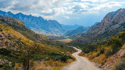 Sticker -   A dirt road lies in a valley surrounded by towering mountains and fluffy clouds above