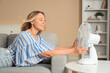 © Pixel-Shot - Beautiful mature happy woman with electric fan lying on sofa at home
