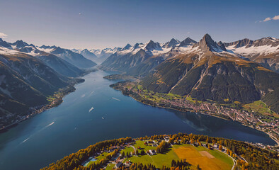 Fototapete - Mountain range with a lake in the middle. The lake is surrounded by trees and houses. The mountains are covered in snow