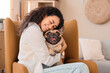 © Pixel-Shot - Happy young African-American woman with cute French bulldog sitting in armchair at home