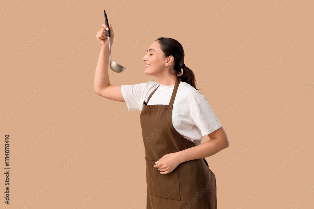 Young woman in apron with ladle on beige background