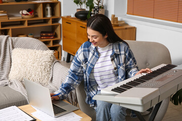 Wall Mural - Beautiful young happy female composer with laptop playing synthesizer at home