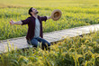 © kamonrat - Farmer Embracing Nature in Paddy Field, Joyful Celebration of Abundance and Connection to Agriculture, Kneeling on Bamboo Pathway Surrounded by Lush Green Rice Plants Under a Clear Sky