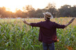 © kamonrat - Farmer Embracing the Sunset in a Cornfield, Enjoying Nature and Serenity, Symbolizing Hope and Gratitude, Standing with Arms Wide Open to the Sky Amid Tall Corn Stalks at Dusk