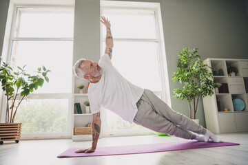 Wall Mural - Elderly man performing side plank exercise on yoga mat indoors in bright daylight