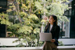 © PaeGAG - Young businesswoman sits with her laptop in a modern office space adorned with lush greenery, looking thoughtfully towards upcoming projects and opportunities