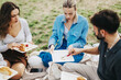 © qunica.com - A group of multiracial friends enjoy a picnic outdoors, sharing food and laughter on a cloudy day. The grassy setting enhances their connection with nature and each other.