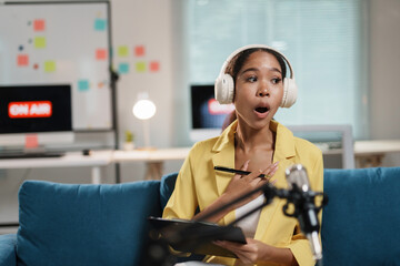 surprised woman wearing headphones and holding clipboard during live broadcast in modern studio