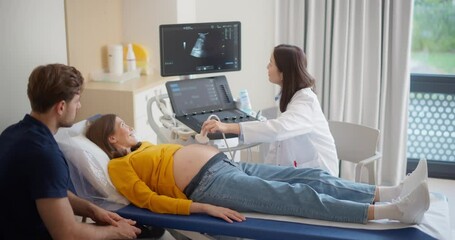 Aufkleber - Caring Female Hospital Obstetrician Conducting an Ultrasound Exam for a Pregnant Woman. Young Couple Watching the Screen while Asian Doctor Describes the Baby’s Growth to Expectant Mother