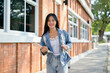 © bongkarn - An attractive Asian female college student stands outdoors at her university, smiling at the camera.