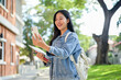 © bongkarn - A happy Asian female college student enjoys a video call while heading to class on campus.
