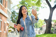 © bongkarn - A happy Asian female college student enjoys a video call while heading to class on campus.