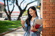 © bongkarn - A happy Asian female college student enjoys a video call while heading to class on campus.