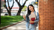 © bongkarn - A female college student stands leaning against a brick building wall, smiling at the camera.