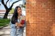© bongkarn - A female student stands leaning against a brick building wall, smiling and looking to the side.