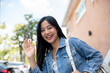 © bongkarn - A beautiful Asian female college student waves and smiles at the camera while standing outdoors.