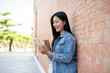© bongkarn - A smiling female student stands leaning against a brick building wall outside, chatting on her phone