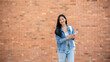 © bongkarn - A smiling Asian female college student holding her smartphone while standing outdoors.