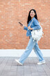 © bongkarn - A side view of a smiling Asian female college student holding her smartphone while walking outdoors
