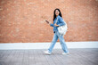 © bongkarn - A side view of a smiling Asian female college student holding her smartphone while walking outdoors