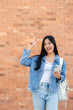 © bongkarn - A smiling woman points at an empty space while standing outdoors with a brick wall in the background