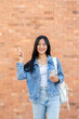 © bongkarn - A smiling woman points at an empty space while standing outdoors with a brick wall in the background