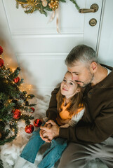 Wall Mural - a father and daughter, hands clasped, sharing a tender embrace near a decorated Christmas tree. Warmth and love radiate from the image