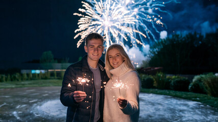 Wall Mural - photo of a couple holding sparklers with fireworks background