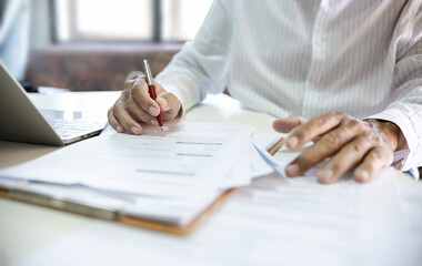 Wall Mural - Asian businessman reviewing document reports at office workplace with computer laptop. legal expert, professional lawyer reading and checking financial documents or insurance contract